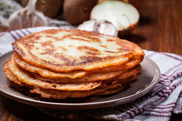Stack of potato pancakes on a wooden table. In the background po