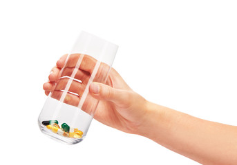 Hand holding glass with pile of different tablets and capsules