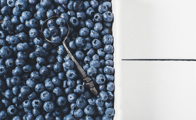 Blueberries on vintage wooden white background top view, healthy food on table mockup, berry for smoothie with spoon on rustic country board, fresh bilberry nutrition mock up closeup, copy space 