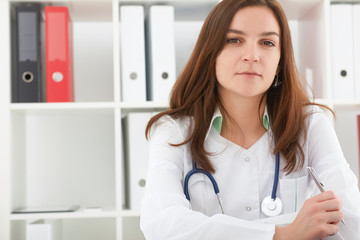 Beautiful female medicine doctor sitting at the table and holding a pen. She  smile and look in camera. Medical care or insurance concept.