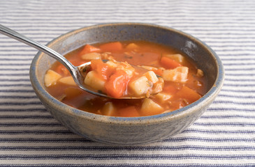 Bowl of Manhattan style clam chowder with spoonful on a striped tablecloth.