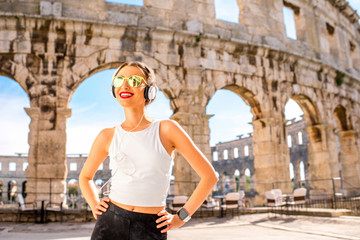 Fototapeta na wymiar Young sports woman with headphones and smartwatch resting after the training near the ancient coliseum in Pula city
