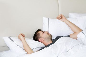 Handsome young man happily sleeping in white bed