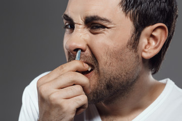 Obraz premium Young handsome man tweezing hair in nose over grey background.
