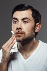 Displeased young man touching face after shaving over grey background.