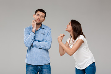 Young beautiful woman angering with man over grey background.