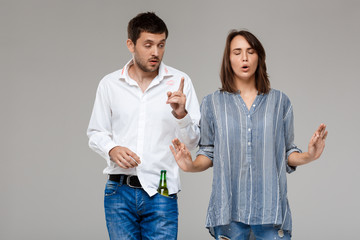 Young woman quarreling, angering with drunk husband over grey background.