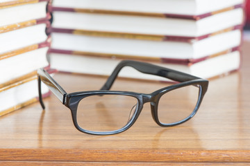 Eyeglasses lying on table with stacks of book in the background. Concept of education, reading literature or studying hard.