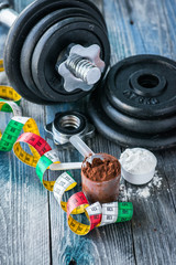 Classic dumbbell with protein powder on rustic wooden table