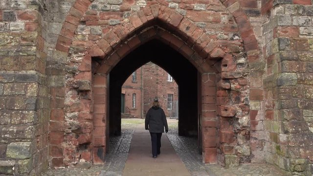 Carlisle England woman walks through castle gate entrance. Border city near Scotland. A Cathedral and castle built in 10th century. Education, trade, commerce and education center.