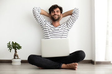 young man sitting down on the floor with laptop and a plant next