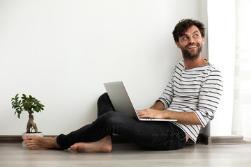 young man sitting down on the floor with laptop and a plant next