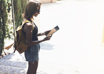 Hipster young girl with backpack using tablet or holding gadget, planning travel. View tourist traveler with sunglasses on background Barcelona. Mock up for text. Vacation journey concept