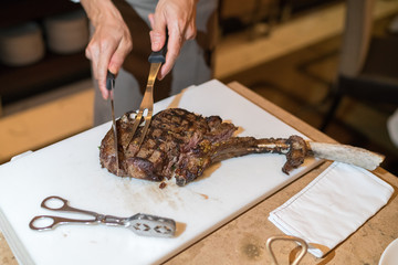 Chef with knife and fork. Professional chef in a restaurant or hotel prepares or cut up t-bone steak.

