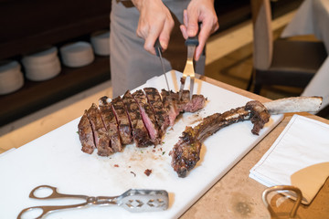 Chef with knife and fork. Professional chef in a restaurant or hotel prepares or cut up t-bone steak.
