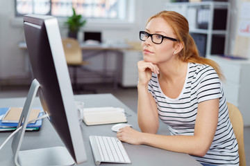 frau im büro schaut nachdenklich auf den pc