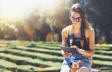 Hipster young girl with backpack and vintage camera using tablet or gadget. View tourist traveler with sunglasses on background Barcelona. Social networking and vacation concept