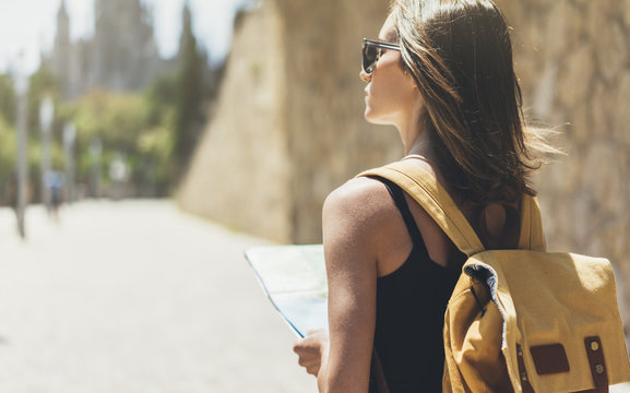 Hipster young girl with bright backpack and sunglasses looking at map. Said view tourist traveler on background sun city, visiting Barcelona. Mock up for text message. Vacation journey concept