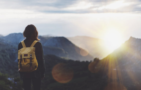 Hipster young girl with backpack enjoying sunset on peak of foggy mountain. Tourist traveler on background view mockup. Hiker looking sunlight flare in trip Spain. Picos de Europa. Journey concept