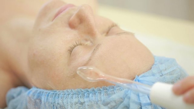 Receiving electric darsonval facial massage procedure. beauty parlor