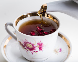 Old-style porcelain kettle pouring tea from jug to cup of tea