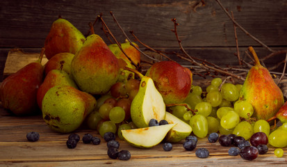 sprig of grapes and a delicious pear on wood background