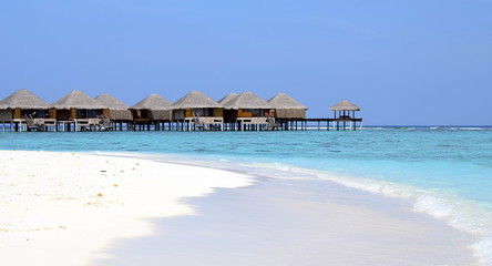 Maldivian beach with white sand, azure water and wooden villas