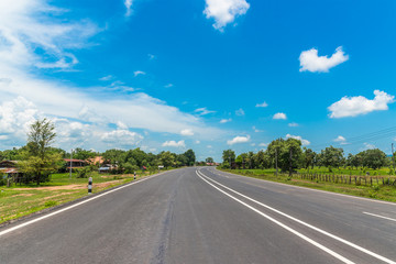 Asphalt road through the countryside and clouds on blue sky