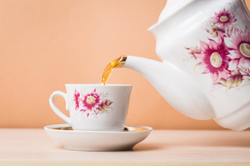 Old-style porcelain kettle pouring tea from jug to cup of tea