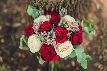Close-up of two wedding rings with bridal flowers on tree trunk covered with moss