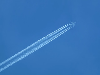 Big four engines passenger supersonic plane flying high in clear cloudless blue sky, leaving long white trace