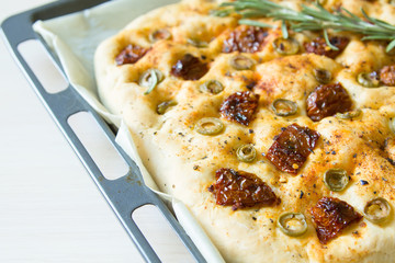 Freshly baked traditional Italian focaccia bread with green olives and sun-dried tomatoes, selective focus