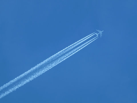 Big four engines passenger supersonic plane flying high in clear cloudless blue sky, leaving long white trace © DyMaxFoto