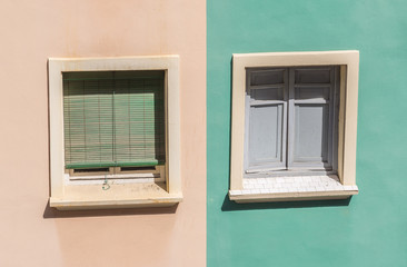 two windows with colorful facade of a residential building shutters and wooden windows orange and green pastel