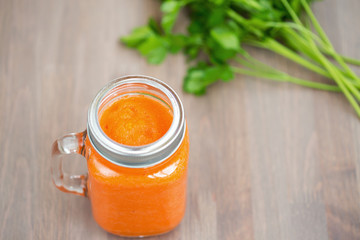 Healthy carrot smoothie in a mason jar with green parsley on wooden background. Shallow dof