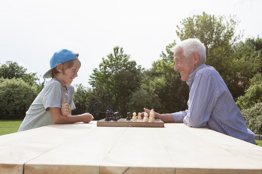 Grandfather and grandson playing chess in garden