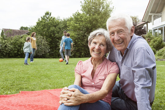 Portrait of happy senior couple with family in background in garden