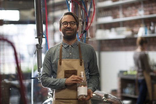 Smiling man holding bottle in distillery
