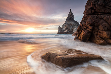 The fiery sky at sunset is reflected on the ocean waves and cliffs, Praia da Ursa, Cabo da Roca, Colares, Sintra, Portugal