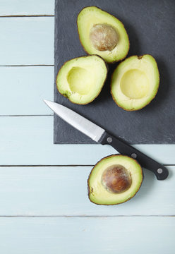 Avocados cut in half on a slate chopping board with a sharp knife