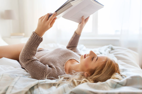 young woman reading book in bed at home