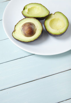 Avocado halves on a plate, on a painted wooden table top background