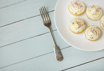 A plate of birthday fairy cakes with vanilla frosting and sprinkles on a painted wooden background