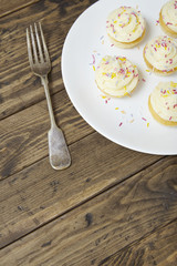 A plate of birthday cupcakes with vanilla frosting and sprinkles on a rustic wooden background with an antique silver fork