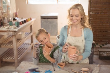 Female potter and girl painting in pottery workshop