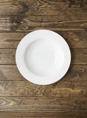 An empty white dinner plate on a rustic wooden background