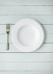 An empty white dinner plate and fork on a shabby chic wooden background