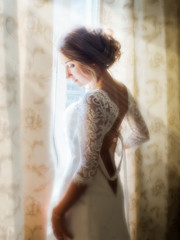 Fototapeta premium a beautiful bride posing in the early morning at the window, soaking up the first rays of the sun