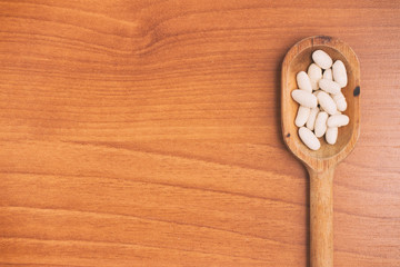  White beans into a spoon over a wooden table. Phaseolus vulgari