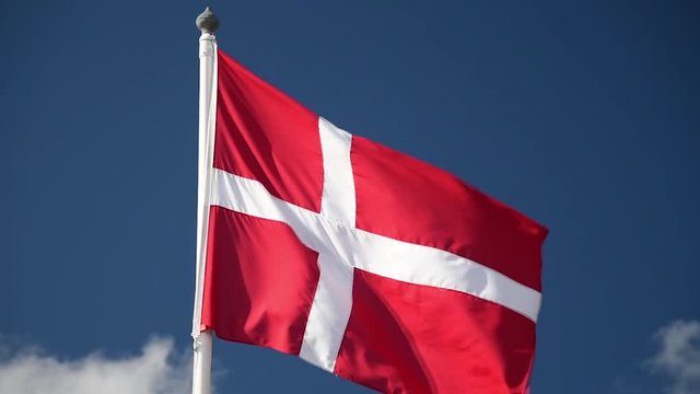 A Danish flag flutters in the wind against a blue sky background